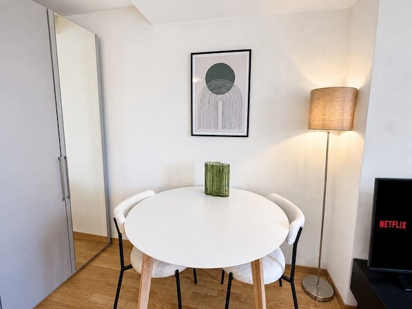 A room with a white round table, a green vase, a framed artwork, a standing lamp, and a TV displaying the Netflix logo. - Studio in a perfect location (Stork 35) (Zürich)
