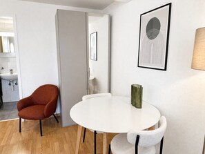 Quarto moderno com uma mesa redonda branca, uma poltrona vermelha e uma obra de arte abstrata emoldurada na parede.