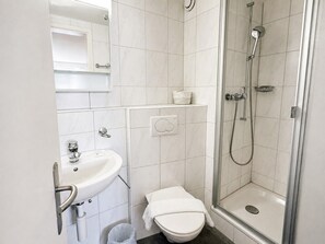 Casa de banho com lavatório branco, sanita e cabine de duche com vidro.