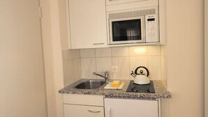 Una cocina compacta con microondas, lavamanos y hervidor en la encimera.