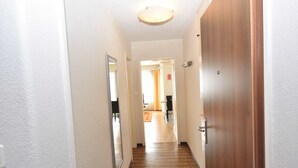 A hallway with a wooden floor and white walls, leading to a room with a door and a mirror on the wall.