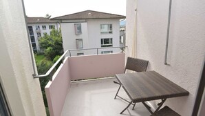 A balcony with a table and chairs, overlooking a residential area with buildings and greenery.