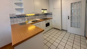 Een compacte keuken met witte kasten, een houten aanrechtblad, een betegelde achterwand en een betegelde vloer.