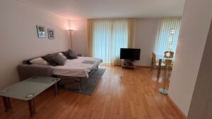 Een moderne woonkamer met een bank, een salontafeltje, een televisie en een eethoek met stoelen.