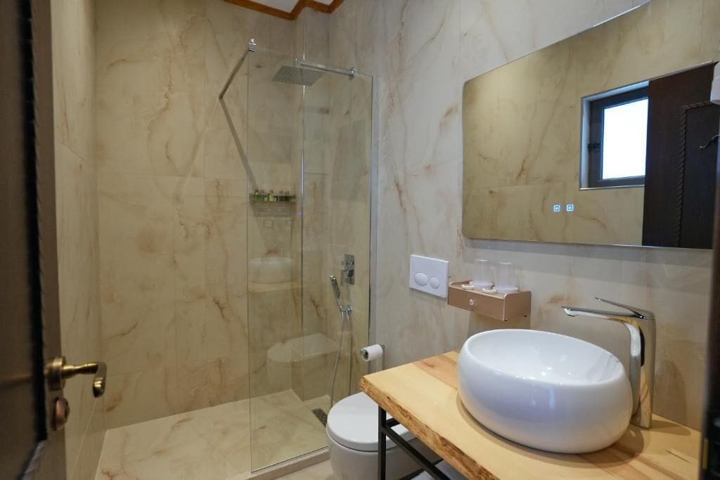Un baño moderno con ducha de vidrio, lavamanos blanco y tocador de madera.