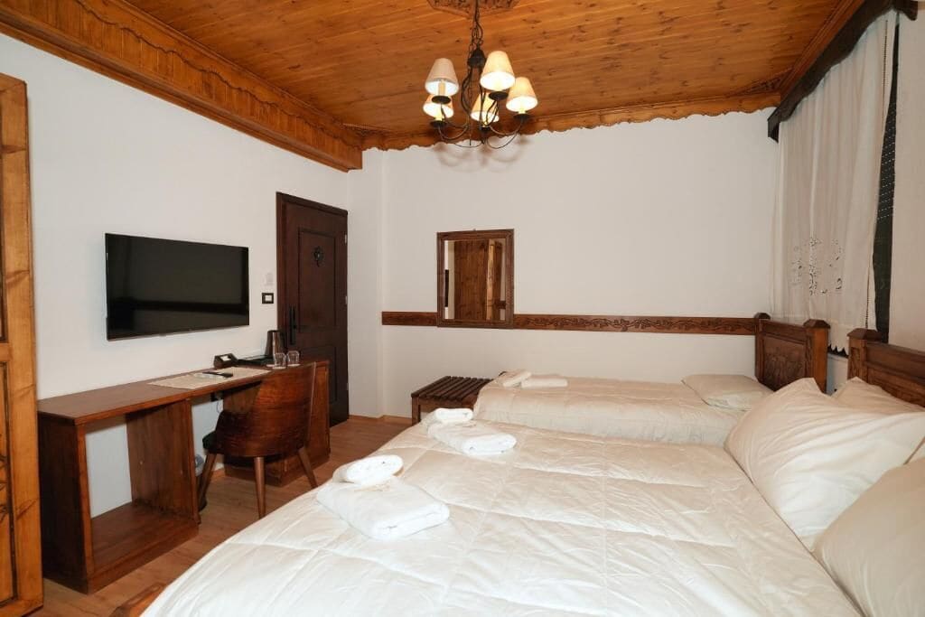 Habitación de hotel con techo de madera, televisor, escritorio, dos camas y un espejo.