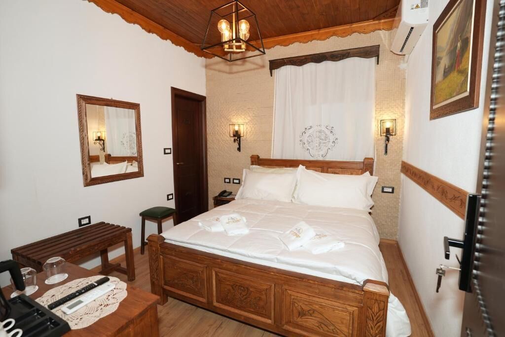 A bedroom with a wooden bed, bedside lamps, a mirror, and a wooden bench.