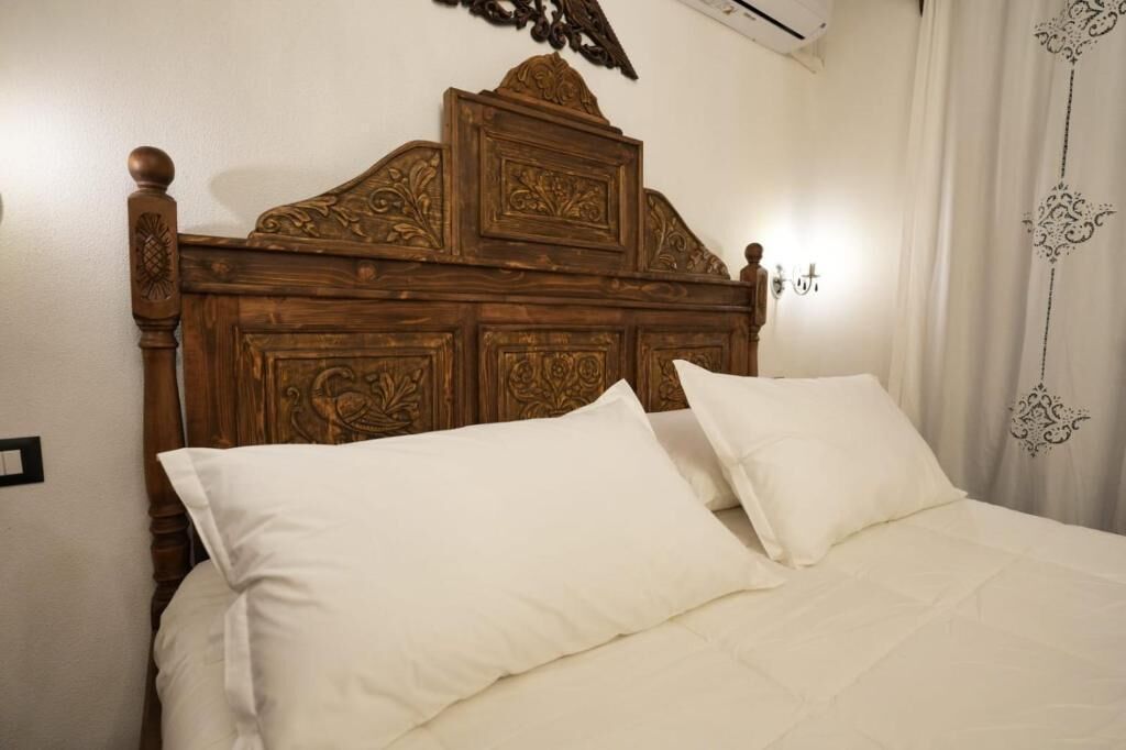 A wooden headboard with intricate carvings, a white bedspread, and a white pillow.