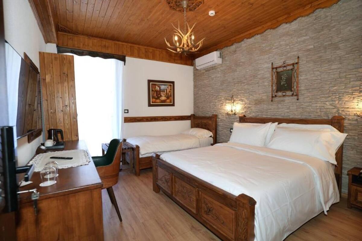 A bedroom with a large bed, two smaller beds, a wooden desk, a chair, and a chandelier.