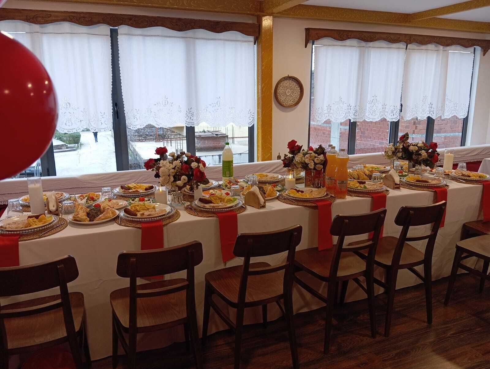 Uma sala de jantar com uma mesa comprida posta para uma refeição, decorada com flores e velas.