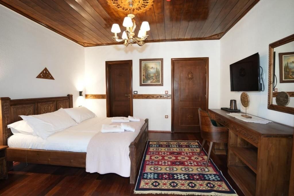 A wooden-framed bedroom with a bed, a desk, a chair, a television, and a patterned rug.