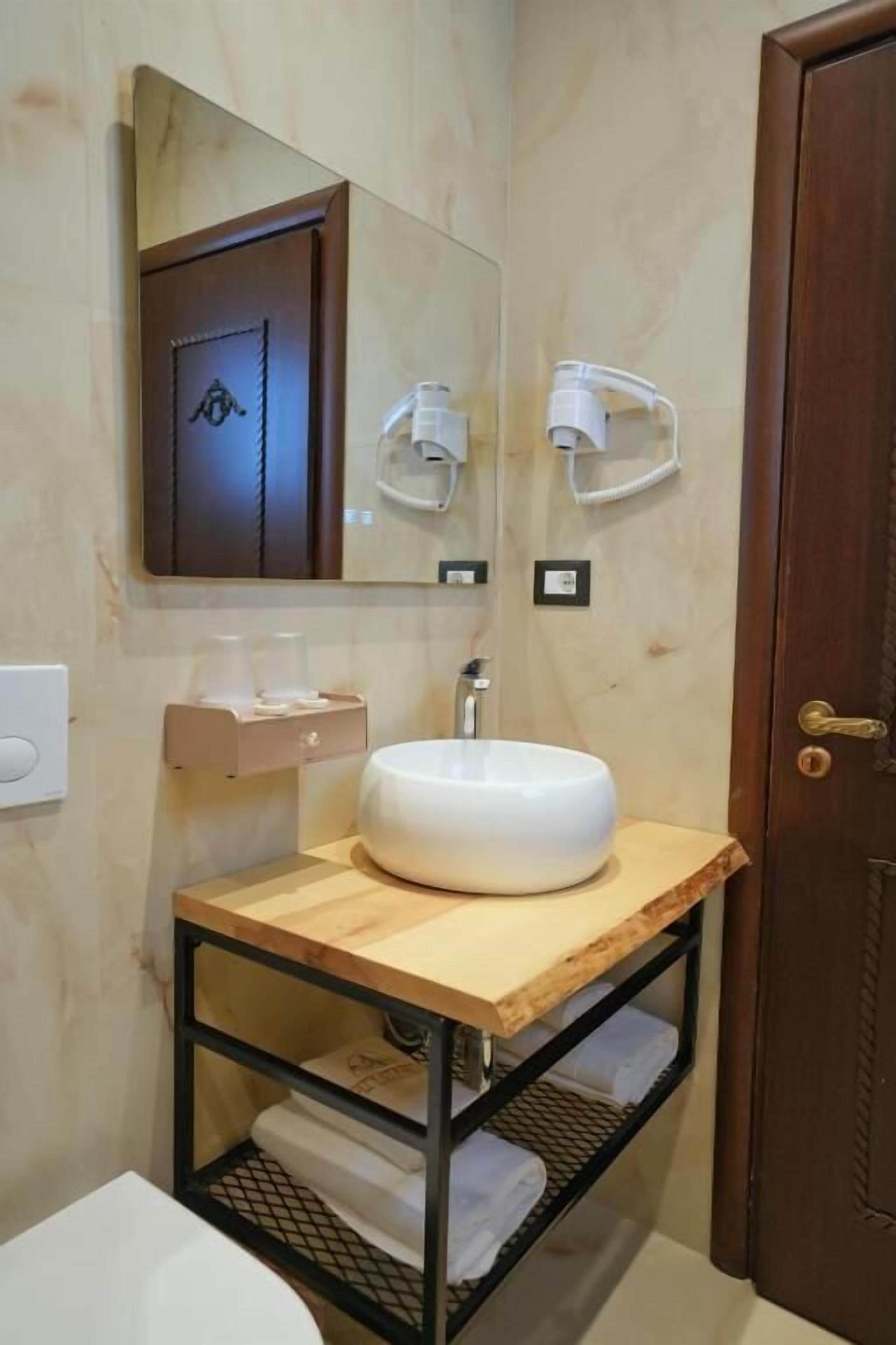 A bathroom with a wooden vanity, a round sink, a towel rack, and a mirror.