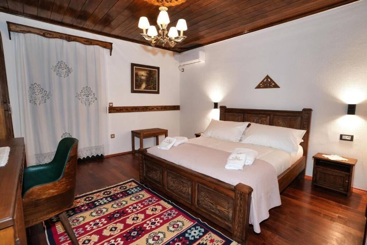 A traditional wooden bed with a headboard, a green upholstered chair, a patterned rug, and a chandelier.