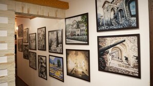 A gallery wall with various framed artworks depicting architectural scenes and historical buildings. - City Street Hotel (Gjirokaster)