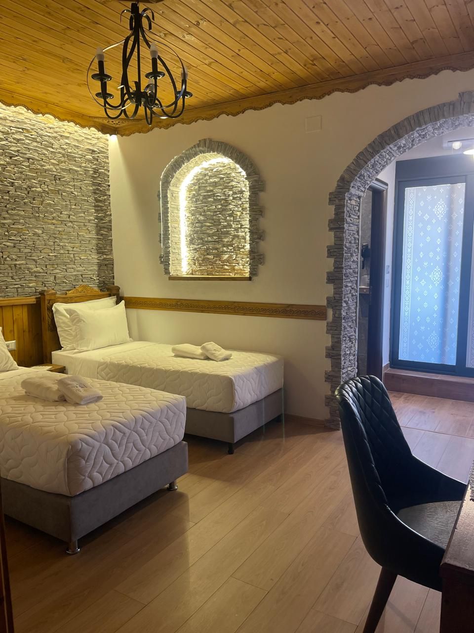 Ein Schlafzimmer mit zwei Betten, einer Kandelaber, Steinwänden und Blick durch ein Fenster.