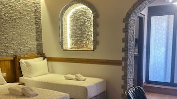 Ein Schlafzimmer mit zwei Betten, einer Kandelaber, Steinwänden und Blick durch ein Fenster.