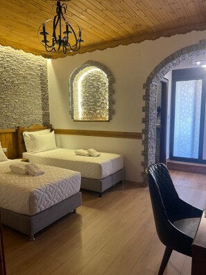 A bedroom with two beds, a chandelier, stone walls, and a view through a window. - City Street Hotel (Gjirokaster)