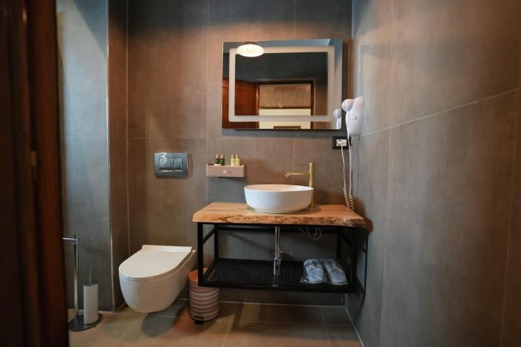Une salle de bain moderne avec des toilettes blanches, un lavabo doté d’un plan de travail en marbre et un miroir au-dessus du lavabo.