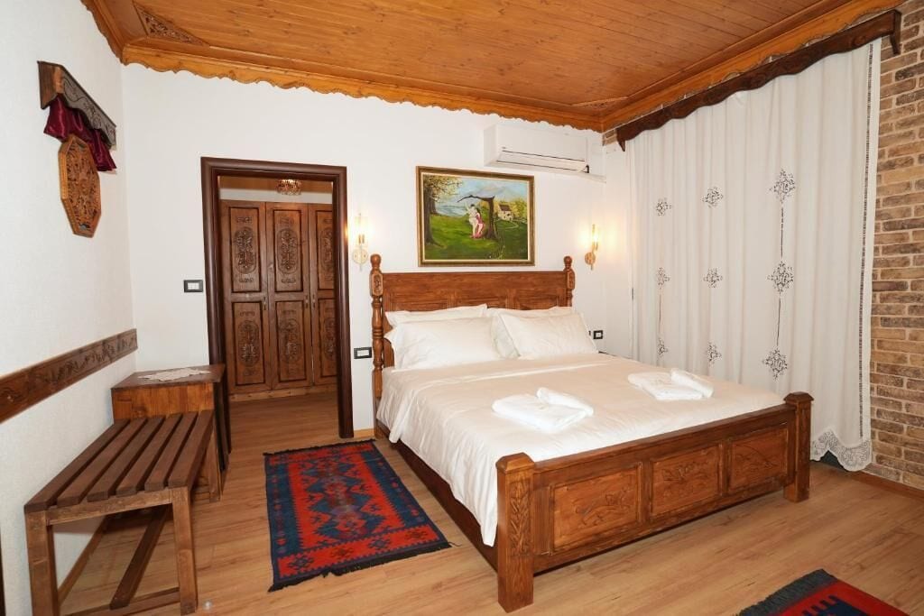 Un dormitorio con una cama de madera, un banco, una alfombra, un cuadro y una puerta.