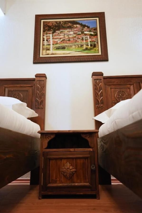 A room with two wooden beds with headboards, a small wooden nightstand, and a framed picture on the wall.
