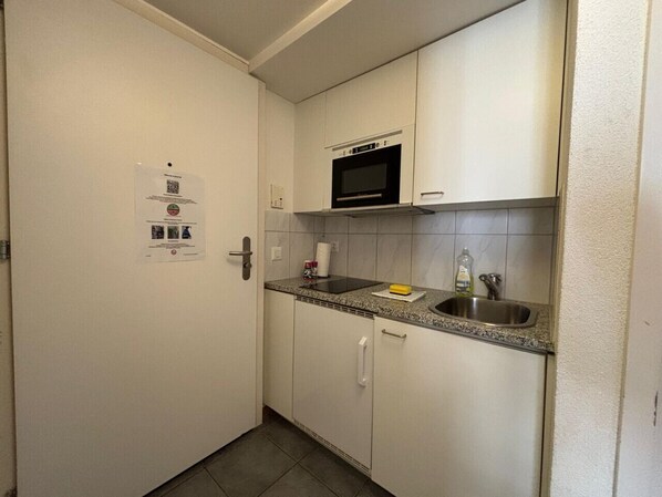Une petite cuisine avec des meubles blancs, un four à micro-ondes, un évier et une porte ornée d’un code QR.