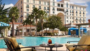A hotel pool area with lounge chairs, a table with drinks, and a large building in the background.