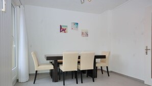 Un comedor con una mesa de madera oscura y seis sillas beige. Hay tres cuadros en la pared.