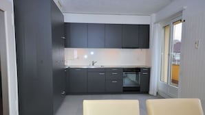 Una cocina moderna con armarios oscuros, una encimera blanca y un comedor con dos sillas.