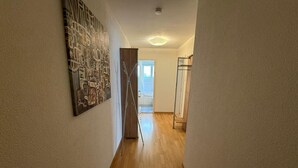 Een hal met een houten vloer, een schilderij aan de linker muur en een deur naar een andere kamer.