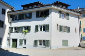 A multi-story building with a white facade and green shutters, featuring a ground-level entrance with a door and a small window. - Loft in the historic district (Symbol 4) (Zürich)