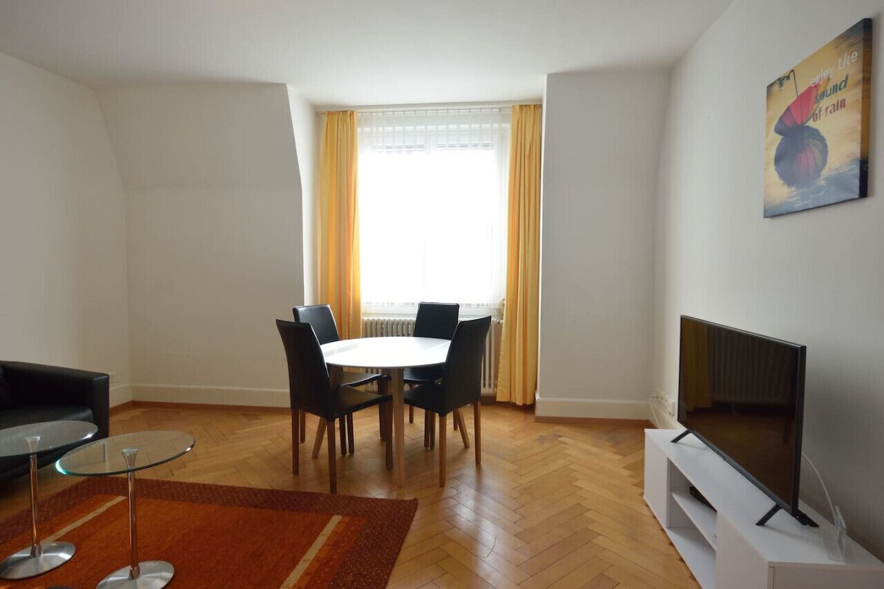 Un salon comprenant une table à manger, des chaises, une table basse en verre, un téléviseur et un tableau accroché au mur.