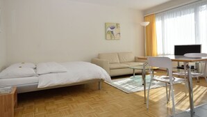 A hotel room with a bed, a sofa, a desk with a chair, a TV, and a painting on the wall. - Very central & bright studio (Vineyard 51) (Zürich)