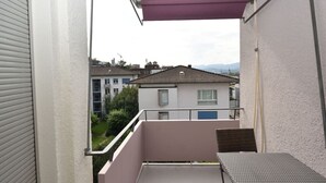 A balcony with a metal table and a chair, overlooking a residential area with houses and a mountain in the background. - Very central & bright studio (Vineyard 51) (Zürich)