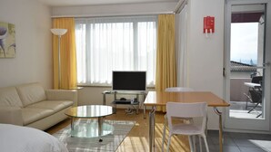 A modern hotel room with a sofa, a glass table, a TV, and a balcony with a table and chairs. - Very central & bright studio (Vineyard 51) (Zürich)
