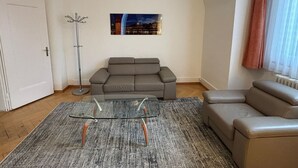 En stue med en grå sofa, et glasbord og en gulvlampe.