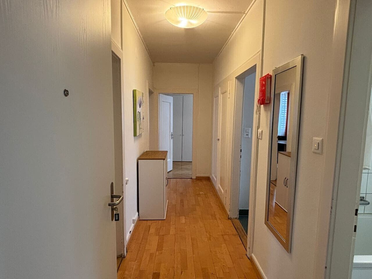 Un pasillo con suelo de madera, paredes blancas y puertas que dan a varias habitaciones.