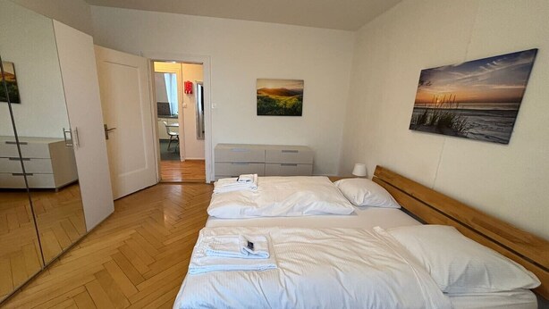 Et hotelværelse med to senge, trægulv, et skrivebord med stol og en dør, der fører til et andet værelse.