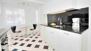 Una cocina moderna con encimera negra, armarios blancos y dos sillas negras.