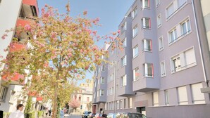 Un edificio residencial de varios pisos con balcones y un árbol con flores rosadas en primer plano.