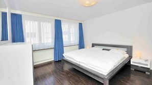 Un dormitorio con cama, una mesita de noche, una ventana con cortinas y una lámpara de techo.