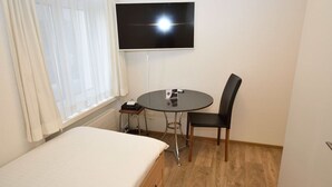 A small room with a bed, a table with a chair, a TV mounted on the wall, and a window with curtains. - Cozy studio near main station (Color 2) (Zürich)