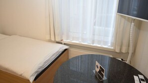 A hotel room with a bed, a round table, and a TV mounted on the wall. - Cozy studio near main station (Color 2) (Zürich)