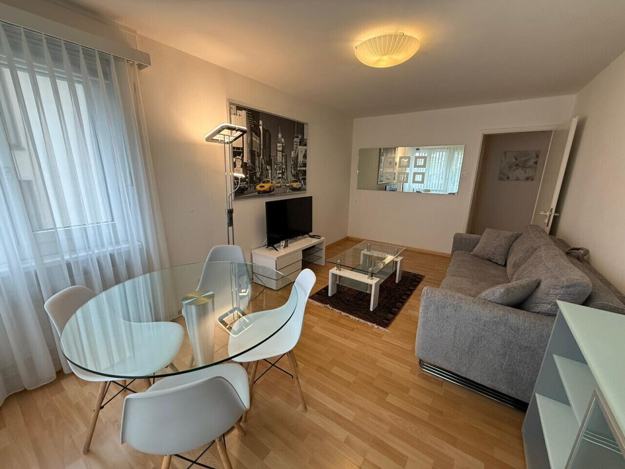 Ein modernes Wohnzimmer mit einem Glastisch, einem grauen Sofa und einem Flachbildfernseher.