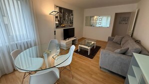 Een moderne woonkamer met een glazen eettafel, een grijze bank en een flatscreen televisie.