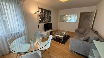 Ein modernes Wohnzimmer mit einem Glastisch, einem grauen Sofa und einem Flachbildfernseher.