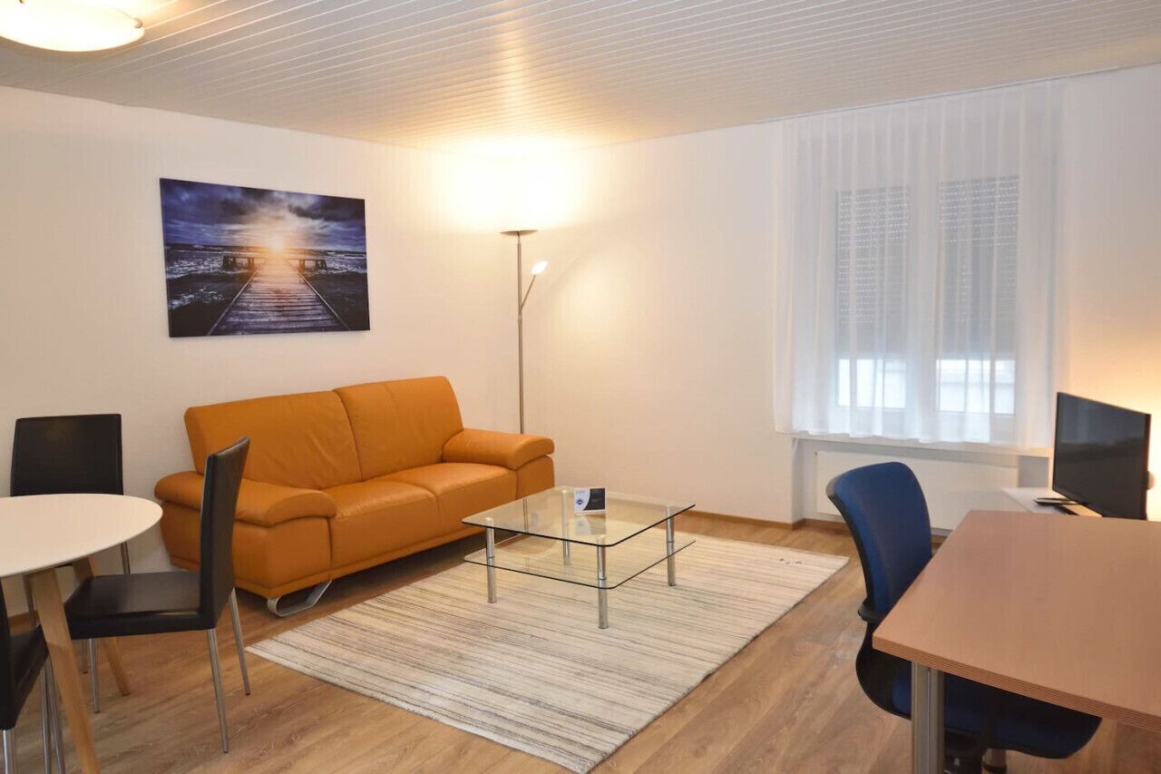 Moderni olohuone, jossa on sohva, lasinen sohvapöytä, ruokapöytä ja televisio.