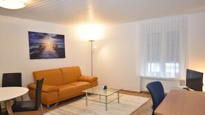 A modern living room with a sofa, a glass coffee table, a dining table, and a TV. - Centrally located 2BR (Color 23) (Zürich)