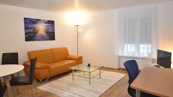 A modern living room with a sofa, a glass coffee table, a dining table, and a TV.