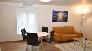 A modern living room with a round dining table, black chairs, an orange sofa, and a glass coffee table. - Centrally located 2BR (Color 23) (Zürich)