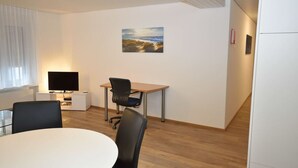 A modern office space with a round table, two black chairs, a desk with a computer, a flat-screen TV, and a painting on the wall. - Centrally located 2BR (Color 23) (Zürich)